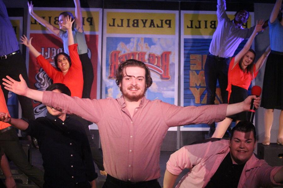 Man with his arms stretched wide smiling in front of performers also stretching their arms up.